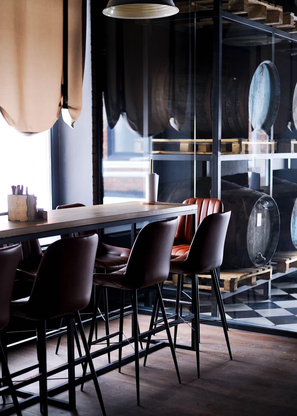 High leather stools at a long table beside barrels racked behind glass