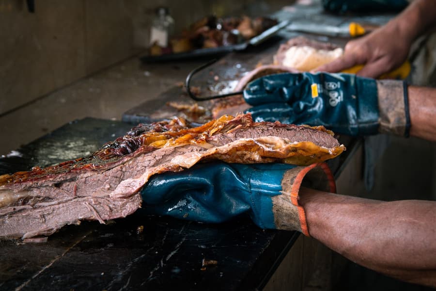 Gloved hands pulling apart a smoked brisket on the block