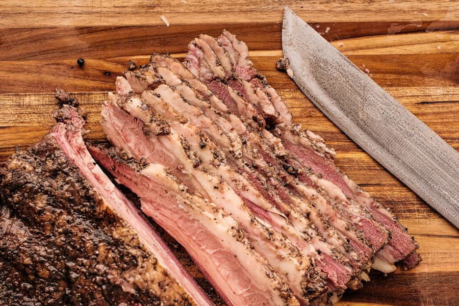 Smoked brisket sliced on a timber board beside the knife
