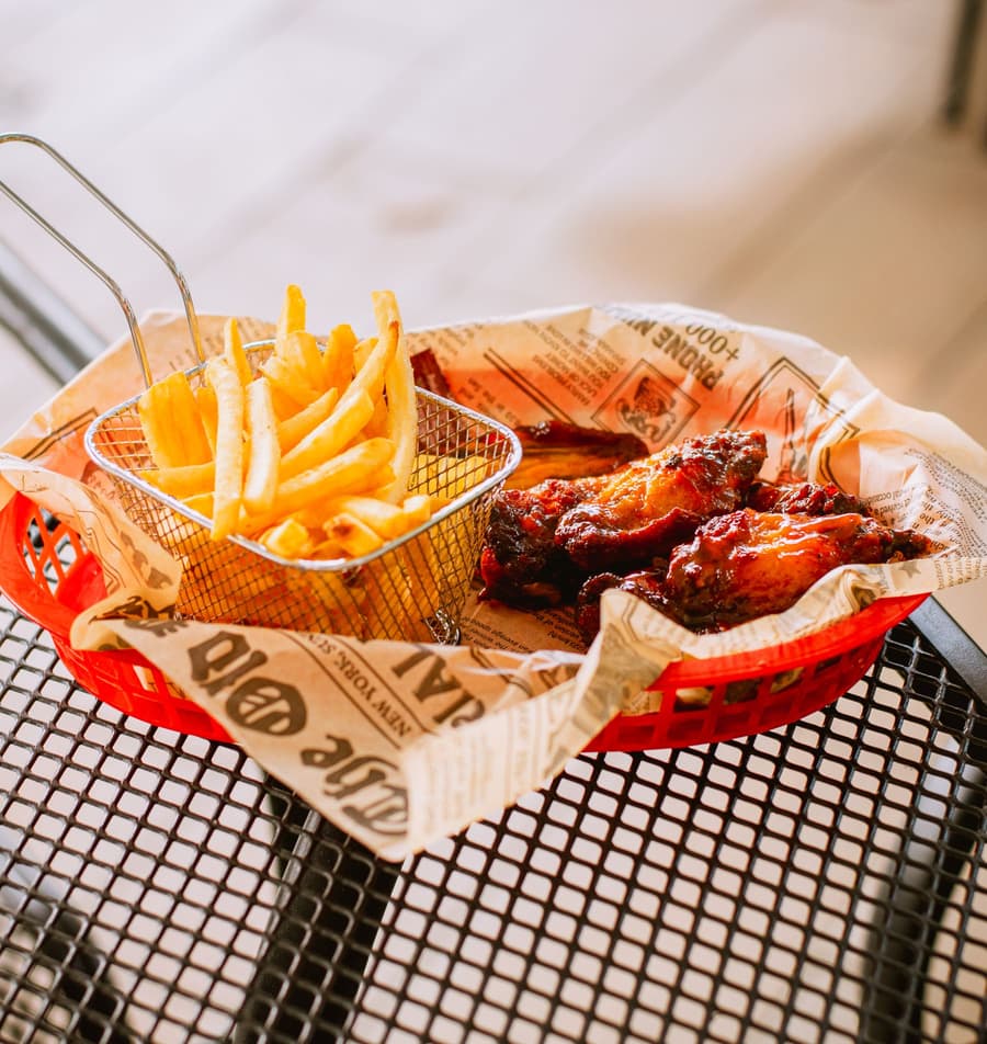 Wings and fries in a wire basket on butcher paper