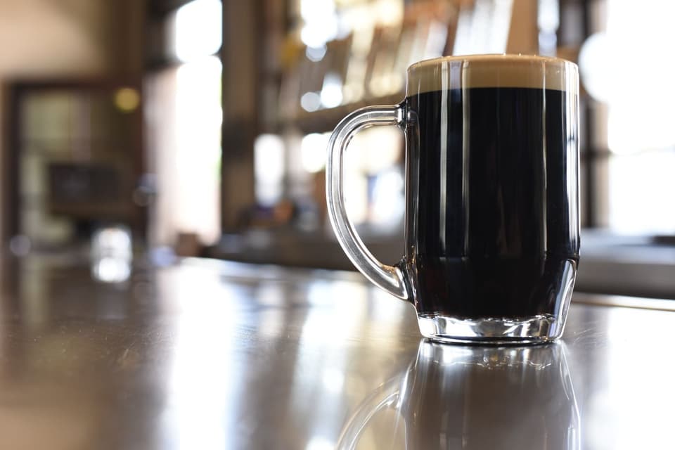 A mug of black stout with a tan head on the bar