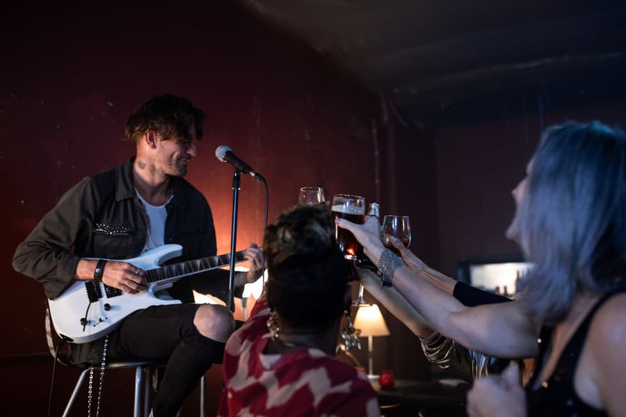 A guitarist on a stool smiling as the front row raises their glasses