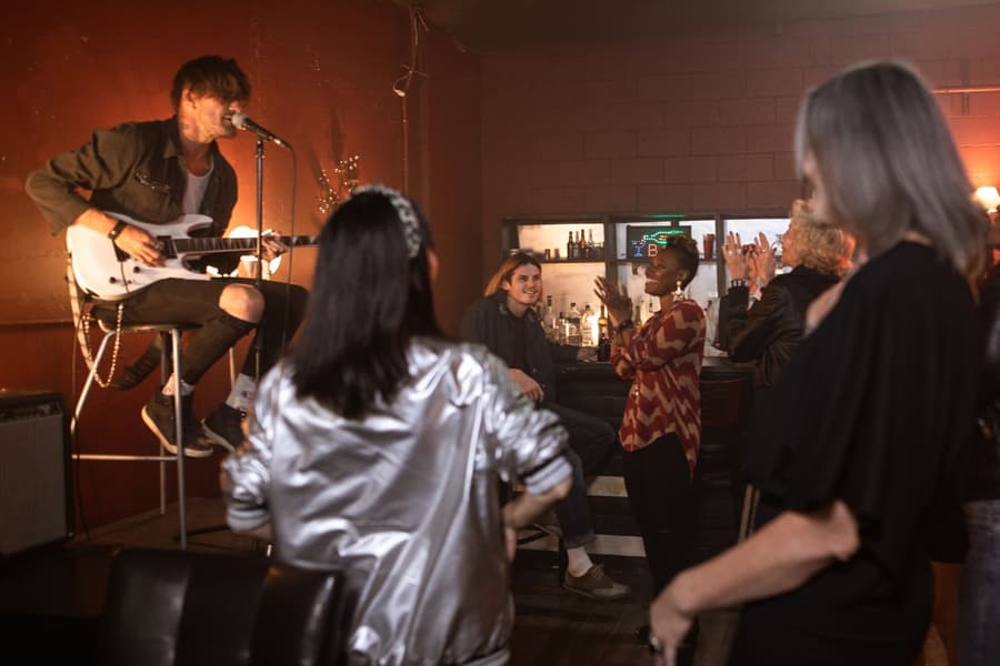 A guitarist singing on a stool while the room claps along